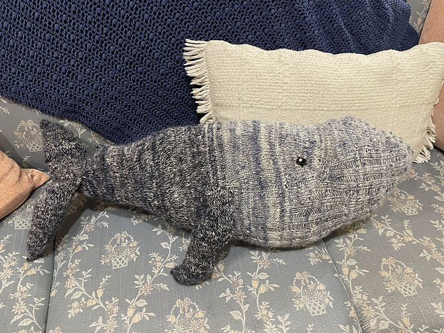 knit whale starting from light blue at the nose and changing to dark blue at the tail, sitting on a light blue patterned couch